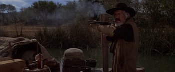 Movie still from “Pat Garrett & Billy the Kid” (1973), directed by Sam Peckinpah – An old man is holding a gun in the water; Medium shot, Low angle