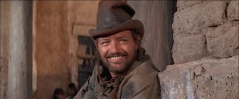 Movie still from “Pat Garrett & Billy the Kid” (1973), directed by Sam Peckinpah – A man in a cowboy hat smiles for the camera; Close Up shot, Low angle