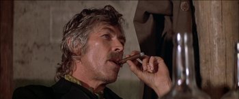 Movie still from “Pat Garrett & Billy the Kid” (1973), directed by Sam Peckinpah – A man is smoking a cigar while looking at the camera; Close Up shot, Low angle
