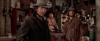 Movie still from “Pat Garrett & Billy the Kid” (1973), directed by Sam Peckinpah – A group of men standing next to each other in a room; Medium shot, Over the shoulder angle