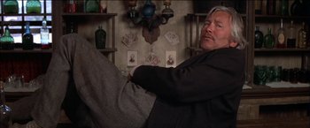 Movie still from “Pat Garrett & Billy the Kid” (1973), directed by Sam Peckinpah – A man sitting on a couch in a room; Medium shot, Low angle