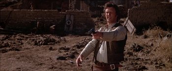 Movie still from “Pat Garrett & Billy the Kid” (1973), directed by Sam Peckinpah – A man holding a gun while standing on a dirt field; Medium shot, Low angle
