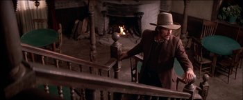 Movie still from “Pat Garrett & Billy the Kid” (1973), directed by Sam Peckinpah – A man wearing a cowboy hat leaning on the railing of a staircase; Medium shot, Low angle