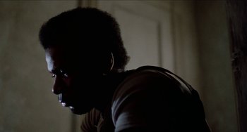 Movie still from “Patty Hearst” (1988), directed by Paul Schrader – A man with a beard is standing in the dark; Close Up shot, Low angle