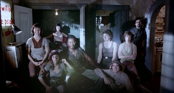 Movie still from “Patty Hearst” (1988), directed by Paul Schrader – A group of people sitting and standing in front of a window; Wide shot, High angle