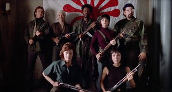 Movie still from “Patty Hearst” (1988), directed by Paul Schrader – A group of men and women holding guns in front of a flag; Medium shot, Low angle
