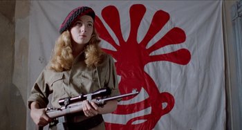 Movie still from “Patty Hearst” (1988), directed by Paul Schrader – A woman holding a rifle in front of a red and white flag; Medium shot, Low angle