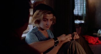 Movie still from “Patty Hearst” (1988), directed by Paul Schrader – A young man looking at his watch while sitting on a couch; Close Up shot, Over the shoulder angle