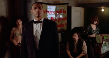 Movie still from “Patty Hearst” (1988), directed by Paul Schrader – A man in a suit standing next to another man in a vest; Medium shot, Low angle