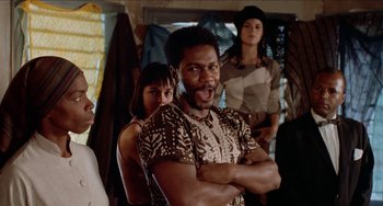 Movie still from “Patty Hearst” (1988), directed by Paul Schrader – A group of people standing next to each other in a room; Medium shot, Low angle