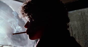 Movie still from “Patty Hearst” (1988), directed by Paul Schrader – A woman is smoking a cigarette in the dark; Close Up shot, Low angle