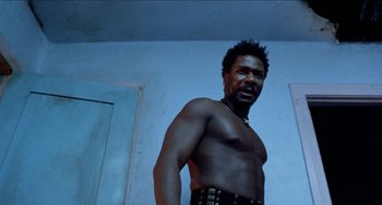 Movie still from “Patty Hearst” (1988), directed by Paul Schrader – A shirtless man in a room with blue walls; Close Up shot, Low angle