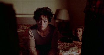 Movie still from “Patty Hearst” (1988), directed by Paul Schrader – A woman sitting on top of a bed next to another woman; Medium shot, High angle
