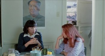 Movie still from “Patty Hearst” (1988), directed by Paul Schrader – Two women sitting at a table in front of a portrait of mao zedong; Medium shot, Over the shoulder angle