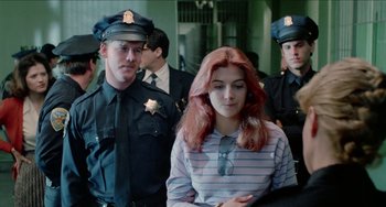 Movie still from “Patty Hearst” (1988), directed by Paul Schrader – A woman in a striped shirt is surrounded by police officers; Medium shot, Over the shoulder angle