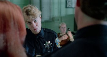 Movie still from “Patty Hearst” (1988), directed by Paul Schrader – A police officer talking to another person in a room; Close Up shot, Over the shoulder angle