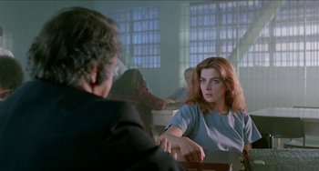 Movie still from “Patty Hearst” (1988), directed by Paul Schrader – A woman sitting in front of a man in front of a window; Medium shot, Over the shoulder angle