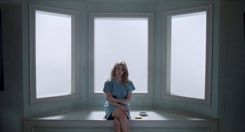 Movie still from “Patty Hearst” (1988), directed by Paul Schrader – A woman sitting on a window sill in a room; Wide shot, High angle