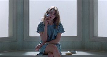 Movie still from “Patty Hearst” (1988), directed by Paul Schrader – A woman sitting on the ground holding a cell phone to her ear; Medium shot, Low angle