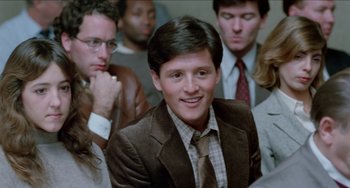 Movie still from “Patty Hearst” (1988), directed by Paul Schrader – A man in a suit and tie smiling; Close Up shot, Low angle