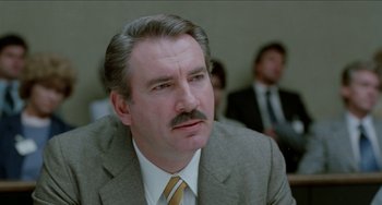 Movie still from “Patty Hearst” (1988), directed by Paul Schrader – An older man with a mustache wearing a suit and tie; Close Up shot, Low angle