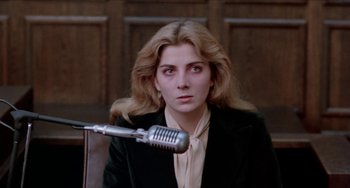 Movie still from “Patty Hearst” (1988), directed by Paul Schrader – A woman in a black jacket is sitting in front of a microphone; Close Up shot, Low angle