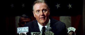 Movie still from “Pearl Harbor” (2001), directed by Michael Bay – An older man in a suit and tie talking into microphones; Close Up shot, Low angle