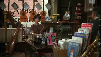 Movie still from “Pennies from Heaven” (1981), directed by Herbert Ross – A woman sitting at a table in front of guitars; Wide shot, High angle