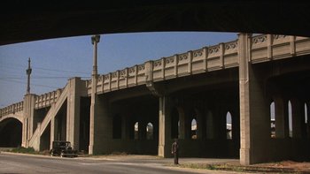 Movie still from “Pennies from Heaven” (1981), directed by Herbert Ross – A person standing under a bridge near a street; Extreme Wide shot, Low angle