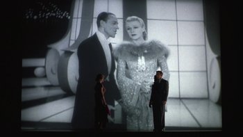 Movie still from “Pennies from Heaven” (1981), directed by Herbert Ross – Two people are standing in front of a large screen; Medium shot, Low angle