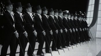 Movie still from “Pennies from Heaven” (1981), directed by Herbert Ross – A group of men in black suits and top hats holding walking sticks; Medium shot, High angle