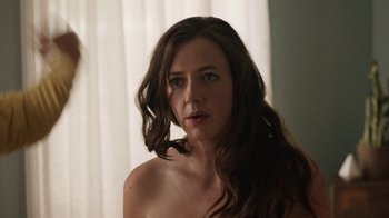 Movie still from “People Places Things” (2015), directed by Jim Strouse – A woman with long brown hair and blue eyes looking at the camera; Close Up shot, Over the shoulder angle