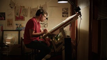 Movie still from “People Places Things” (2015), directed by Jim Strouse – A man sitting in front of an easel drawing; Medium shot, Low angle