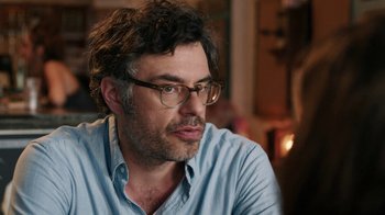 Movie still from “People Places Things” (2015), directed by Jim Strouse – A person wearing glasses and a blue shirt; Close Up shot, Over the shoulder angle