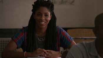 Movie still from “People Places Things” (2015), directed by Jim Strouse – A young woman sitting at a table smiling for the camera; Close Up shot, Over the shoulder angle