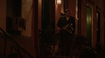 Movie still from “People Places Things” (2015), directed by Jim Strouse – A man standing on a porch holding a dog; Wide shot, Over the shoulder angle