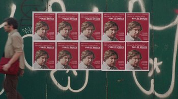 Movie still from “People Places Things” (2015), directed by Jim Strouse – A bunch of posters of a man on the side of a wall; Wide shot, High angle
