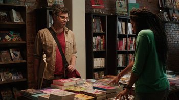 Movie still from “People Places Things” (2015), directed by Jim Strouse – A man and a woman standing in front of a table full of books; Medium shot, Over the shoulder angle