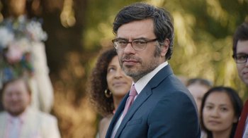 Movie still from “People Places Things” (2015), directed by Jim Strouse – A person wearing a suit and glasses; Close Up shot, Over the shoulder angle