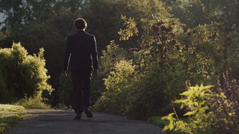 Movie still from “People Places Things” (2015), directed by Jim Strouse – A man walking down a path near a forest; Wide shot, Over the shoulder angle