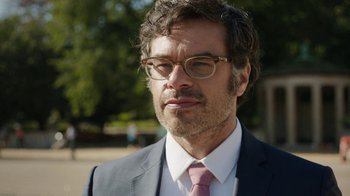 Movie still from “People Places Things” (2015), directed by Jim Strouse – A person wearing glasses and a suit; Close Up shot, Over the shoulder angle