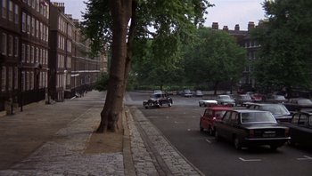 Movie still from “Performance” (1970), directed by Donald Cammell – Cars are driving down the street near a large tree; Extreme Wide shot, High angle