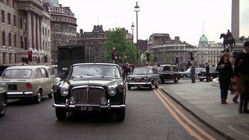 Movie still from “Performance” (1970), directed by Donald Cammell – An old car is driving down the street; Wide shot, Low angle