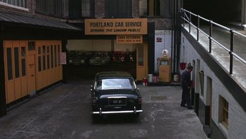 Movie still from “Performance” (1970), directed by Donald Cammell – An old car parked in front of the portland car service building; Extreme Wide shot, High angle
