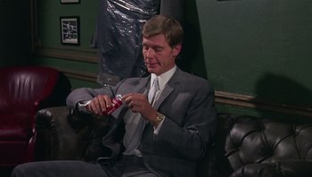 Movie still from “Performance” (1970), directed by Donald Cammell – A man in a suit and tie holding a bottle of toothpaste; Medium shot, Low angle