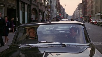 Movie still from “Performance” (1970), directed by Donald Cammell – A man in the back seat of a black car; Medium shot, Over the shoulder angle