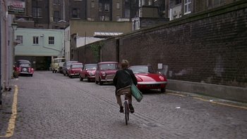 Movie still from “Performance” (1970), directed by Donald Cammell – A man riding a bike down a street past parked cars; Wide shot, High angle