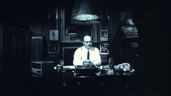 Movie still from “Performance” (1970), directed by Donald Cammell – A man sitting at a desk in front of a typewriter; Medium shot, Low angle