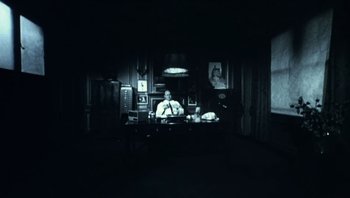 Movie still from “Performance” (1970), directed by Donald Cammell – A man sitting at a desk in a dark room; Wide shot, High angle