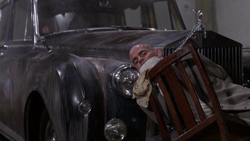 Movie still from “Performance” (1970), directed by Donald Cammell – A man holding a chair in front of an antique car; Wide shot, Low angle